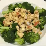 A bowl of Chicken Salad Chick-style broccoli salad, featuring fresh broccoli florets, shredded cheese, crispy bacon bits, raisins, and a creamy dressing.