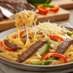 A plate of Philly steak pasta with steak strips, sautéed peppers, onions, and melted cheese.